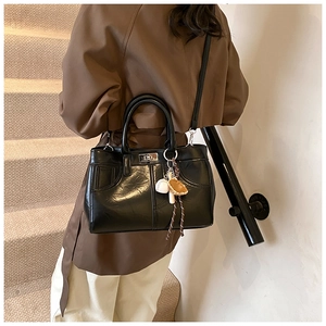 Détail du sac Kelly en cuir brillant noir avec fermoir argenté et breloque de baseball