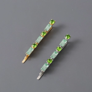 Detailed close-up of gold and silver hair clips with sparkling green emerald cut stones