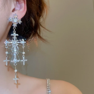 Detailed view of silver cross earrings with pearls and crystals on a model