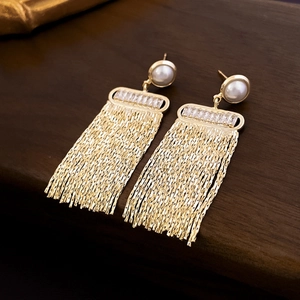 Close-up of gold chain tassel earrings with pearls and zircon on dark wood surface