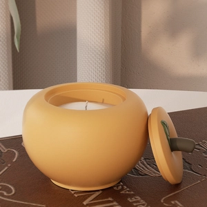 Detail van een oranje keramische kaarsenpot in de vorm van een kaki met groen bladdeksel