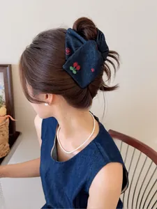 Détail d'une pince à cheveux en denim avec broderie cerise portée par un modèle