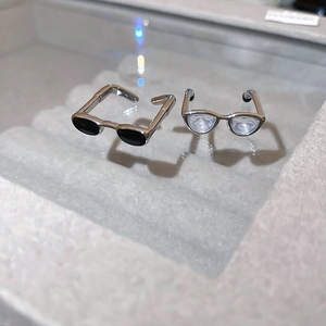 Macro shot of silver metal glasses-shaped rings with black and clear lenses on tray