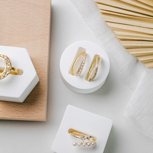 Modern gold rings set with pearls and zircons on white plaster and wood base