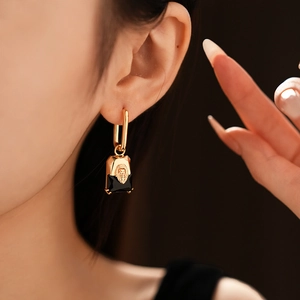 Close-up of a gold lion head earring with a black square gemstone on a model ear