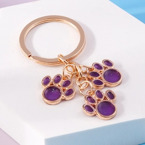 Macro detail of glitter purple cat paw charms on a gold keychain with geometry backdrop
