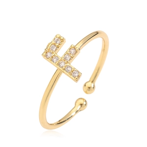 Close-up of golden adjustable ring with letter F design and clear gemstones