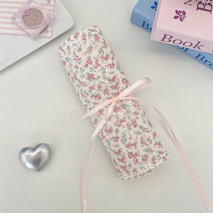 Detail of floral makeup brush roll bag with pink ribbon bow on a decorative desk