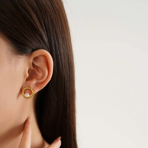 Macro shot of gold-plated twisted rope earrings featuring a central crystal on model ear