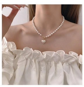Close-up of pearl necklace featuring a golden heart pendant and T-bar toggle clasp