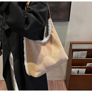 Woman in black coat carrying khaki suede tote bag with white faux fur trim in cozy room