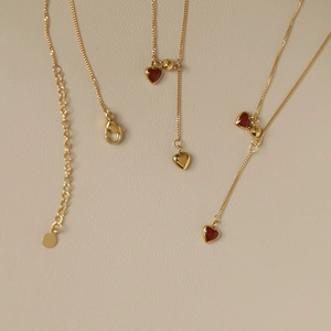 Macro view of gold-plated heart pendant with deep red enamel and lobster clasp chain