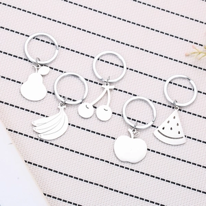 Set of 5 cute silver stainless steel fruit keychains on a striped fabric background