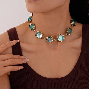 Detail of vintage gold necklace featuring blue resin gems and leaf-pattern metal setting