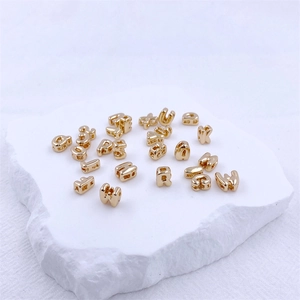 Close-up of golden bubble alphabet charms for DIY jewelry on a white textured surface
