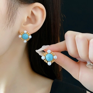 Close-up of vintage gold earrings with turquoise stone and small pearls on model