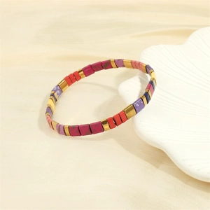 Macro shot of colorful Tila bead bracelet with gold accents on a white shell plate