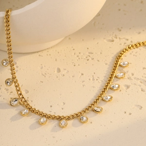 Detail of gold fringe necklace with water-drop crystals on a textured surface