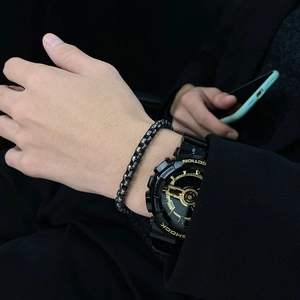 Close-up of a men's black beaded bracelet and a sport watch with gold dial accents