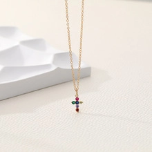 Detail of a golden double-layered snake chain necklace with a colorful gemstone cross