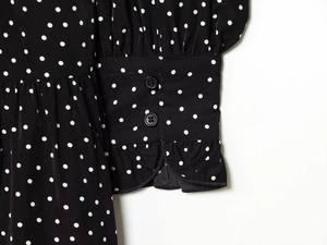 Detailed macro view of black polka dot dress featuring ruffled cuffs and decorative buttons