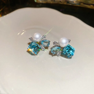 Detail of silver stud earrings with blue square crystal, pearl, and pave diamonds