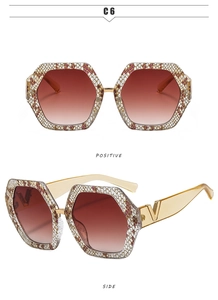 Detail of oversized hexagonal sunglasses with red gradient lenses and golden V-leg design