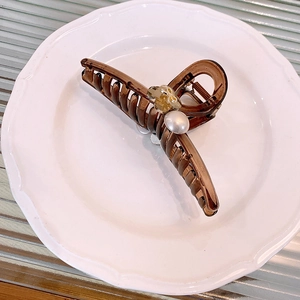 Detail of amber hair claw with crystal bow and large pearl on a white ceramic plate
