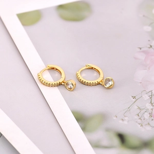 Detailed close-up of golden hoop earrings with round zircon charms and micro-pave setting
