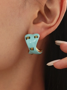 Close-up of light blue enamel C-shaped earrings with gold polka dots worn by a model