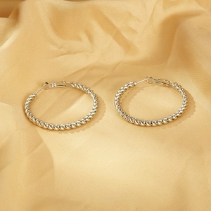 Detailed view of silver twisted rope hoop earrings on luxury champagne silk fabric