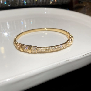Close-up of gold plated zircon bangle on a white ceramic tray with bokeh lighting