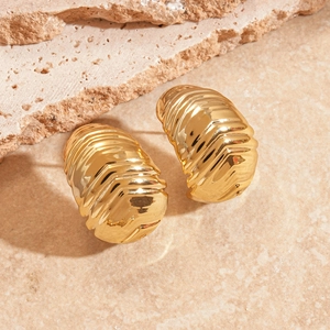 Vue macro de boucles d'oreilles croissant dorées à texture nervurée sur pierre beige