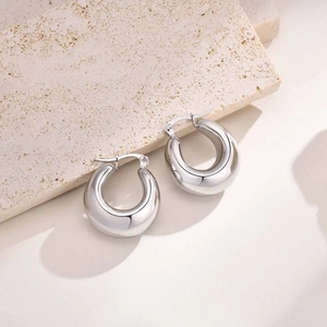 Close-up of chunky silver hollow hoop earrings with a polished mirror finish on stone