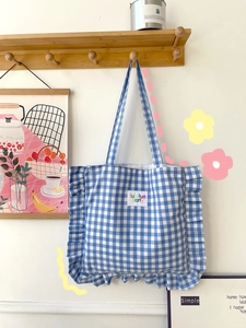 Blue plaid canvas tote bag with ruffle trim and fun fun party label on a wooden hook
