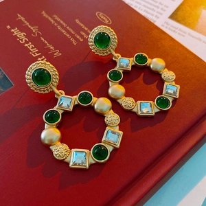 Vintage gold hoop earrings with green gemstone and crystal on a red book backdrop
