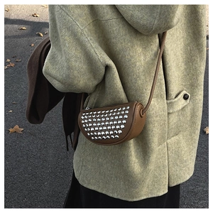 Detail view of a brown rivet half-moon crossbody bag styled with a green tweed coat
