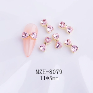 Pink heart-shaped crystal bow nail charms 11x5mm with gold base on a manicured nail
