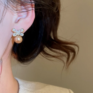 Macro shot of silver bow stud earring with sparkling zircons and large golden pearl