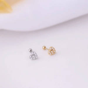Macro detail of heart-shaped screw back earrings in gold and silver with zircon inlays