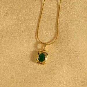 Detail of gold snake chain with emerald green stone pendant and micro diamond accents