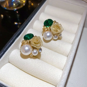 Vue macro de boucles d'oreilles rose dorée avec gemmes vertes et perles en écrin