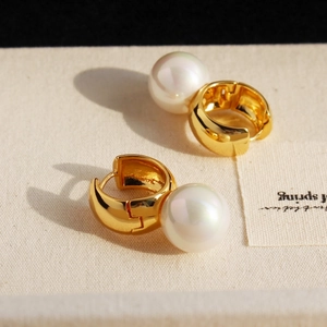 Elegant gold hoop earrings with large round pearls on a textured cream background