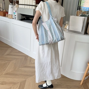 Close-up of floral canvas tote bag with lace detail worn on a shoulder in a cafe