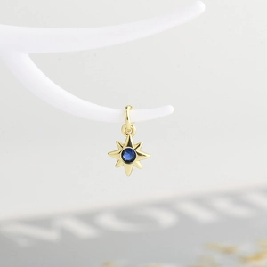 Detailed view of a gold starburst pendant with a center blue zircon on a jewelry stand