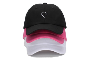 Détail de casquettes empilées en noir, rose et blanc avec broderie de cœur délicate
