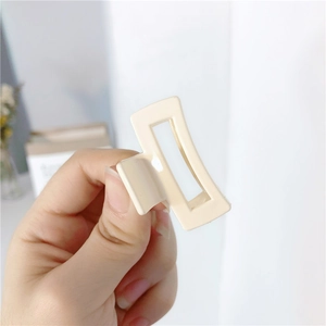 Detail shot of a glossy cream rectangular hair claw clip held in hand with spring mechanism