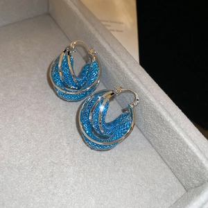 Macro detail of blue woven mesh inside silver hoop earrings on grey velvet display