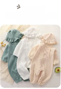 Flat lay of soft cotton gauze baby rompers with matching ruffled hats in earth tones