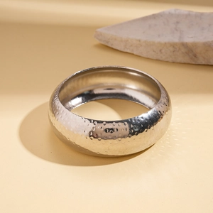 Detail of silver wide hammered metal cuff bracelet with textured surface on a stone prop
